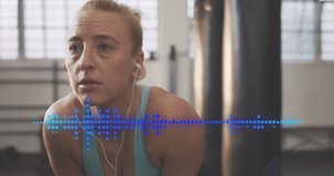 Animation of audio meter over caucasian woman in gym wearing earphones. Music, exercise, health and fitness concept digitally generated video.