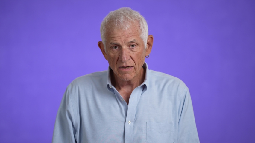 Slow motion portrait of sad upset worried disturb displeased shocked elderly gray-haired man 70s wears blue shirt sigh surprise put hands on face isolated on solid purple background studio | Shutterstock HD Video #1094717801