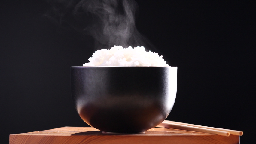 Japanese rice, Cooked rice. Close up natural steaming cooked Japanese white rice in black bowl with chopstick on black background, soft focus. Healthy Food Concept. Royalty-Free Stock Footage #1094719355