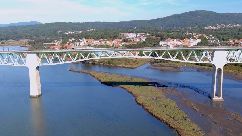 Railway bridge over the ulla river, the village and industrial buildings and the forested mountains in the sunny blue sky orizonte, drone shot down, Catoira, Galicia, Spain | Shutterstock HD Video #1094725459