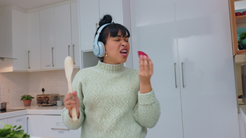 Woman in kitchen eating strawberry, listen to music with headphones and dancing. Girl with healthy fruit play radio, with earphones and dance, while cooking smoothie or salad while relax in home Royalty-Free Stock Footage #1094729883