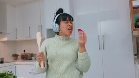 Woman in kitchen eating strawberry, listen to music with headphones and dancing. Girl with healthy fruit play radio, with earphones and dance, while cooking smoothie or salad while relax in home - Powered by Shutterstock - Get 15% off with code: PIKWIZARD15