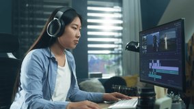 Female asian freelancer editing video for customer or travel blogger in program on computer while sitting at the table and working at home
