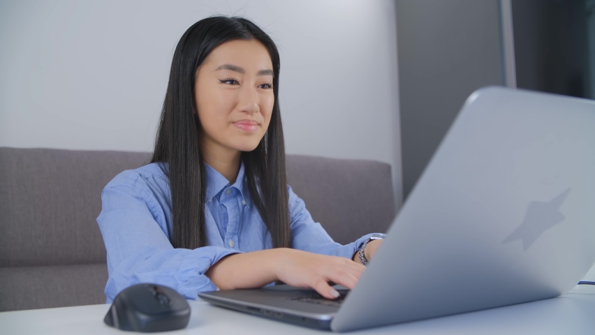 Happy Asian girl coding on laptop at home. Cheerful young Vietnamese woman typing text on modern notebook computer. Royalty free video clip of freelancer female person working at home  | Shutterstock HD Video #1094735861