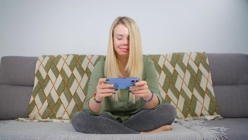 Young woman playing mobile game app on modern smarphone. Gamer person plays video game on phone. White female using mobile phone to play games online with happy smile
