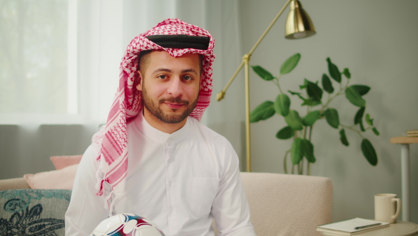 Middle eastern football fan portrait. Young man holding soccer ball, guy supporting favorite team. Wearing traditional Islamic male clothes. Worship and culture concept. | Shutterstock HD Video #1094737139