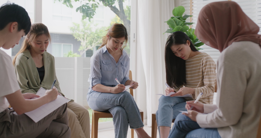Young adult asia team Gen Z group sit circle fill paper form note idea in stress relief class. Woman worker people work at office mental health care center social issue sharing in rehab club session.