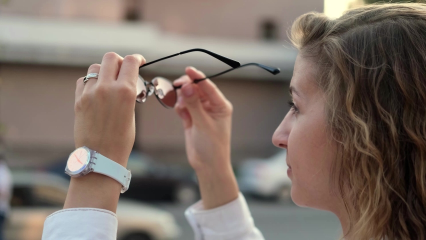 Young attractive woman looks through stylish sunglasses putting them on in the sun close-up outdoors. Beautiful dreamy face enjoying relaxing, contemplating happiness on a sunny day