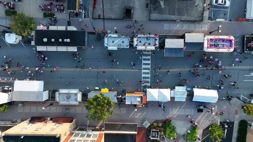Top down aerial of people enjoying town fair on street. Games of chance and food stands. Carnival family entertainment in USA.