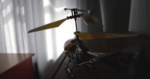 Point of view video of toy yellow radio-controlled model helicopterflying and landing on children's desk with drawings, pencils and scissors. Window is in the background. Slow motion 50 fps