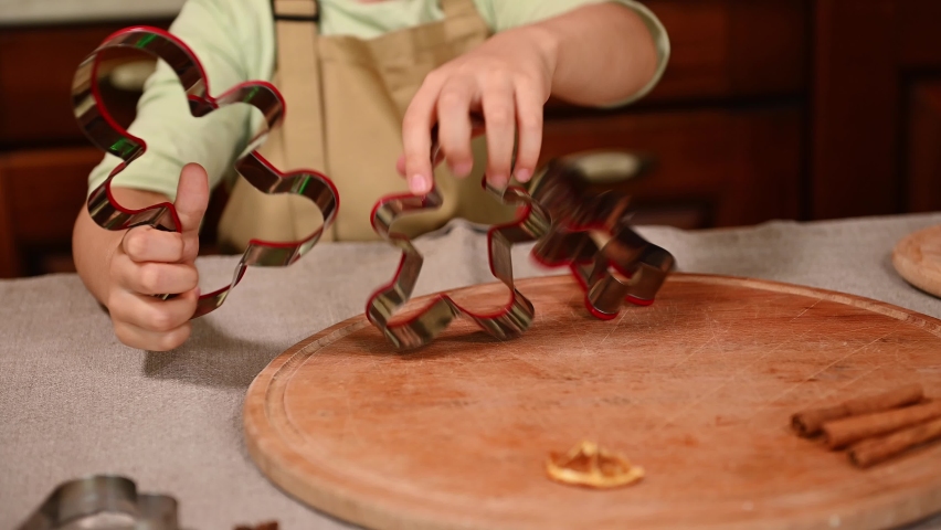 Selective focus on gingerbread cookie cutters in the hands of a pretty little girl, wearing a beige chef