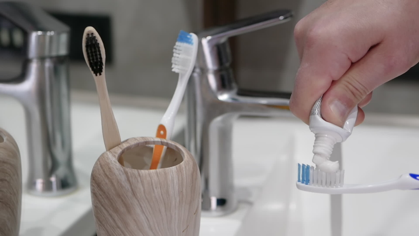 Squeezing toothpaste onto a toothbrush in the bathroom