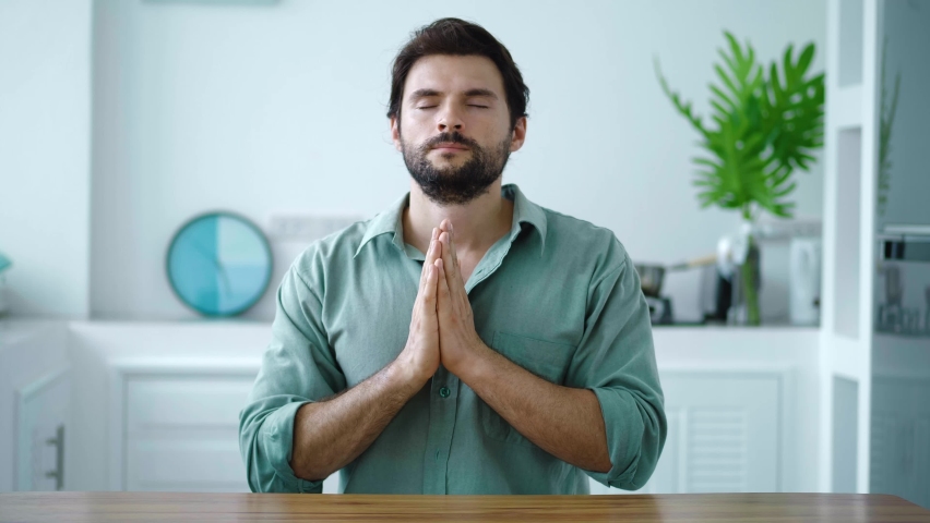 Charming serene Hispanic guy prays to God, holding hands at chin level, whispering a prayer, then assuming a meditation pose, taking deep breaths, trying to relax. Mindfulness. Spiritual growth | Shutterstock HD Video #1094752859