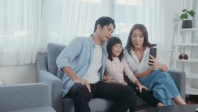 Asian family with children holding smartphone and making video call at home

