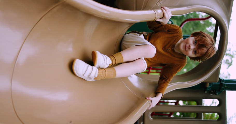 excited redhead kid having fun, going down the slide at the playground in the park