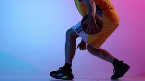 Dribbling ball. Professional basketball player training with basketball ball at studio over gradient blue pink neon background. Sport, action, motion, skill concept.
