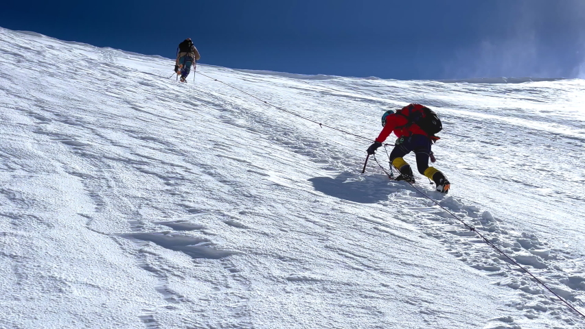 4K two mountaineers climbing steep snowy slope tied together with rope using pickaxes. Mountaineering, climbing, alpinism concept. Royalty-Free Stock Footage #1094764561