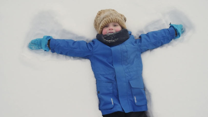 Top view of glad child doing snow angel. Little boy playing in snowdrift and having fun with fresh snow. Active outdoors leisure for kids on nature in snowy winter day. Royalty-Free Stock Footage #1094768341