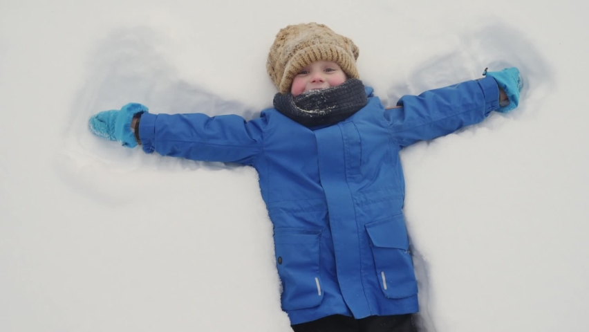 Top view of glad child doing snow angel. Little boy playing in snowdrift and having fun with fresh snow. Active outdoors leisure for kids on nature in snowy winter day. Royalty-Free Stock Footage #1094768341