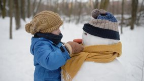 Little boy building snowman in snowy park. Child puts hat and scarf on snowman . Active outdoors leisure with family with children in winter. Kid during stroll in a snowy winter park - Powered by Shutterstock - Get 15% off with code: PIKWIZARD15