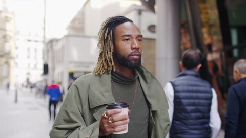 Attractive and confident young black man walking through the city drinking from a coffee cup, in slow motion Video Stok