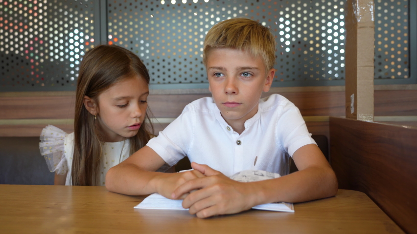 Caucasian boy and girl relaxing with cartoon book, cute siblings sitting enjoy reading book at cafe while waiting for their order. | Shutterstock HD Video #1094769799