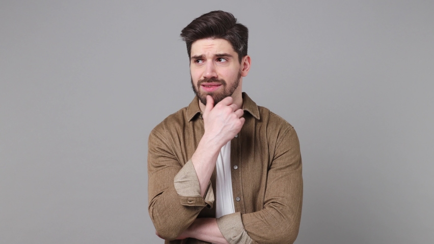 Young puzzled thoughtful pensive gloomy man 20s he wear brown shirt look aside put hand prop up on chin iterates over solution options isolated on plain grey background studio People lifestyle concept | Shutterstock HD Video #1094772777