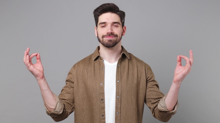 Young spiritual tranquil man 20s he wear brown shirt hold spread hands in yoga om aum gesture relax meditate try to calm down isolated on plain grey background studio portrait People lifestyle concept | Shutterstock HD Video #1094772803