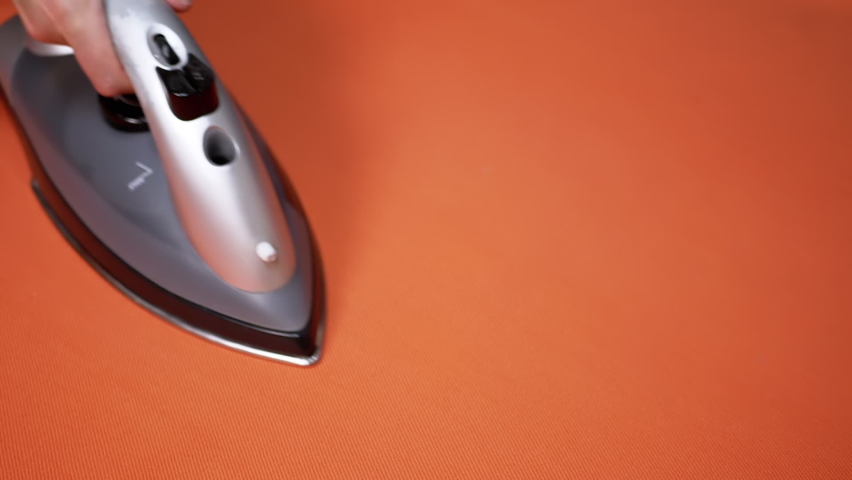 Female Hand Ironing a Bright Orange Cloth with a Steam Iron on an Ironing Board. Close-up. Routine housework. Duties of a hostess. Orange background. Textile. Modern steamer, steam iron. Slow-motion. | Shutterstock HD Video #1094773305