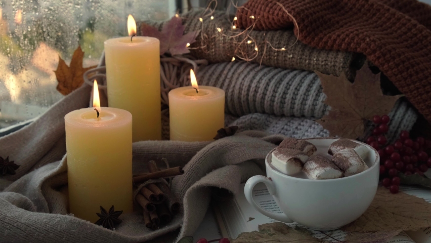 Thanksgiving and Hello Fall, celebrating autumn holidays at cozy home on the windowsill Hygge atmosphere Autumn leaves, spices and candle on cozy knitted sweater in warm yellow lights. Raining Outside | Shutterstock HD Video #1094779381