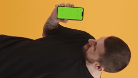 Handsome bearded man shows smartphone with green screen and looks at the camera vertical video studio shot medium shot . High quality 4k footage