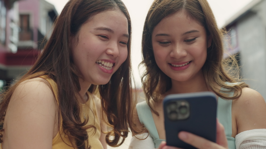 Young Gen Z asia people trending influencer teen girl look at phone enjoy read review and watch viral video laugh joy play social media app post share online fun standing in modern city relax outside.