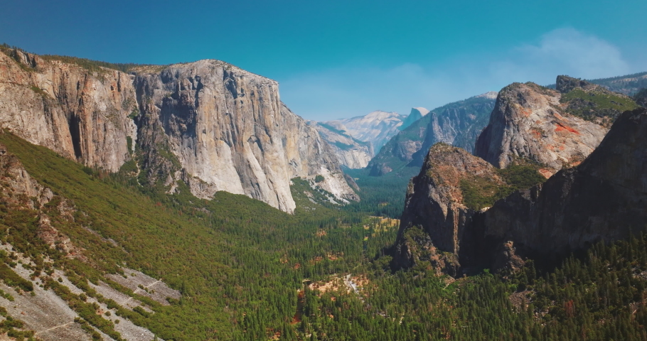 Enormous steep rocks in Yosemite National Park, California, USA. Green pine tree forests growing between the cliffs. Sunny day footage.