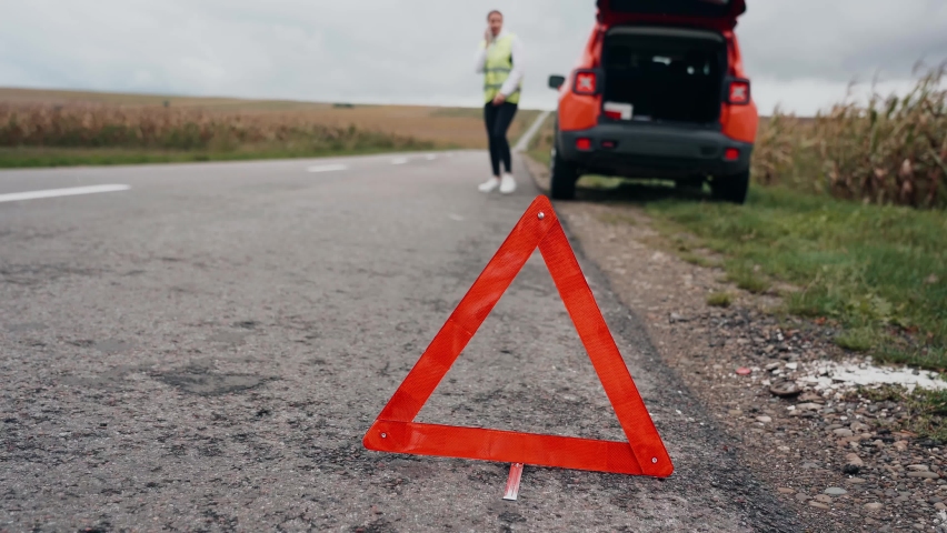 A frustrated woman stands near a broken  down car in the middle of the highway  Breakdown and repair of the car Waiting for help Car service Car breakdown on road 4k
