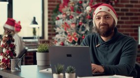 Portrait of project manager with santa hat working on laptop during christmas holiday season. Using computer in office filled with xmas tree and festive decorations, winter ornaments. - Powered by Shutterstock - Get 15% off with code: PIKWIZARD15