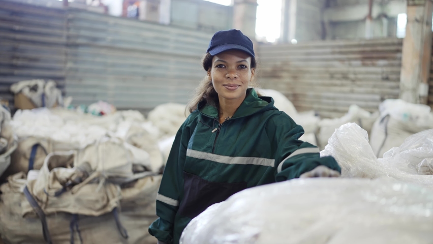 An African-American woman in a special uniform sorts polyethylene at a waste recycling plant. Processing of raw materials, recycling. Pollution control | Shutterstock HD Video #1094790719