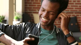 Video call, headphones and a black man with phone, talking and looking out of window. Technology, communication and conversation, a happy African guy chatting on smartphone with earphones and a smile