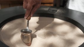 Preparation of Turkish coffee on the sand, close-up, 4k live video. Street cafe, professional barista prepares coffee by hand in a traditional way