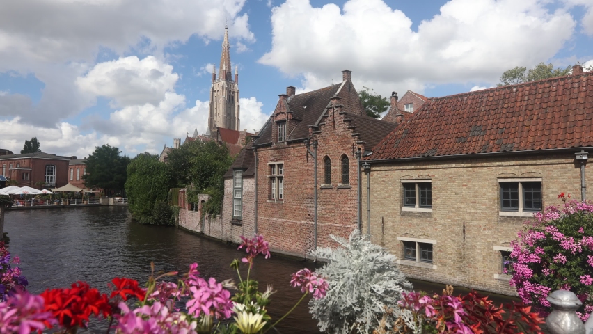 Canal of Bruges and stone buildings during summer day with view of flowers in bloom.