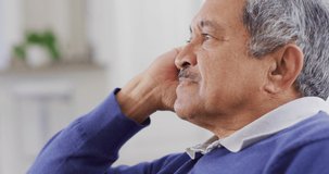 Video of thoughtful senior biracial man looking away, leaning head on hand and smiling. Retirement, healthcare, inclusivity and senior lifestyle concept.