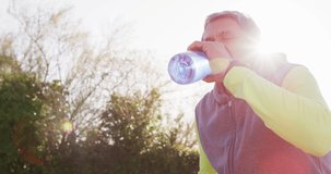 Video of senior biracial man in sports clothes drinking water in sunny street. Retirement, hobbies, health, inclusivity and active senior lifestyle concept.