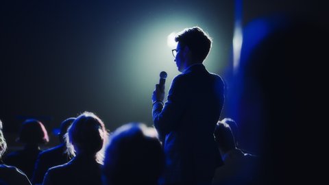 Male Asking a Question to a Speaker During a Q and A Session at an International Tech Conference in a Dark Crowded Auditorium. Young Specialist Expressing an Opinion During a Global Business Summit. 库存视频