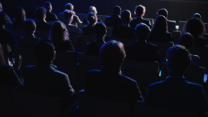 Crowd of Smart Tech People Applauding in Dark Conference Hall During a Motivational Keynote Presentation. Business Technology Summit Auditorium Room Full of Delegates. Footage from Behind. Royalty-Free Stock Footage #1094794973