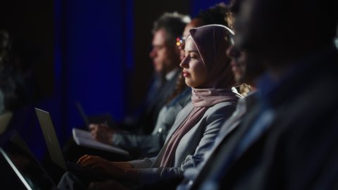 Arab Female Sitting in a Dark Crowded Auditorium at a Human Rights Conference. Young Muslim Woman Using Laptop Computer. Activist in Hijab Listening to Inspiring Speech About Global Initiative. 스톡 비디오