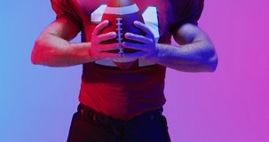 Video of portrait of caucasian american football player with ball over neon purple background. American football, sports and competition concept.