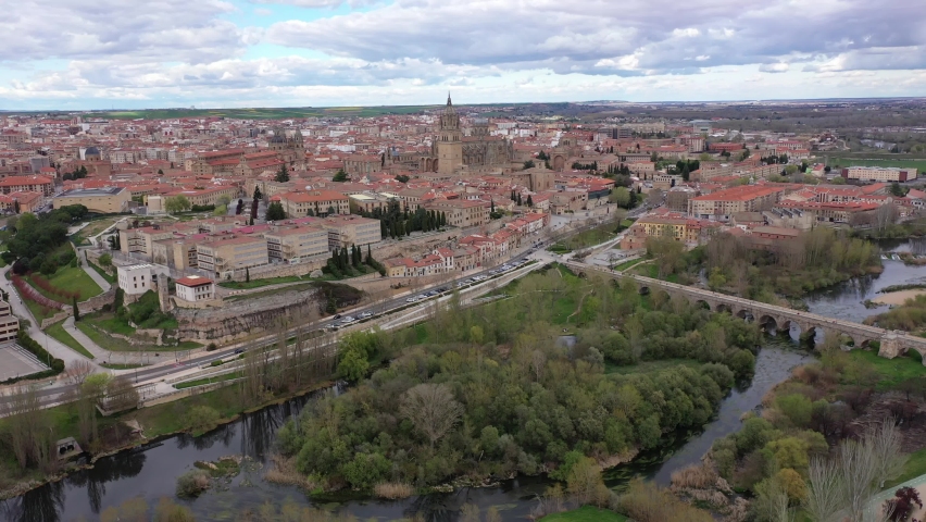 Scenic aerial view of Salamanca historic district overlooking gothic building of cathedral towering over residential buildings and ancient arched roman bridge across Tormes river in spring, Spain