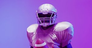 Video of african american american football player with ball over purple neon background. American football, sports and competition concept.
