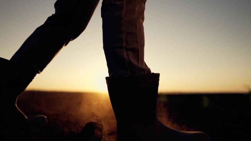 Agriculture. farmer at sunset walk on fertile soil. Farm worker silhouette. The foot of a man in rubber boots walk through the mud. Farmer agronomist works on land plot at sunset. Agriculture concept Royalty-Free Stock Footage #1094800297