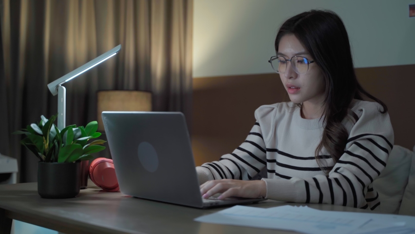 Young Asian woman working casually on a laptop at night in a dark room. Work at home, new normal, Freelance working, home isolation concept. | Shutterstock HD Video #1094802749