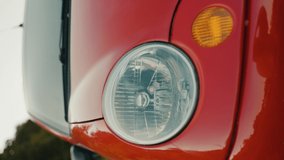 Vertical video. Red car flashes its headlights. Checking functionality of headlight. Bright light of lamps in car's headlights. Detail of machine that improves driving conditions of machine in dark.